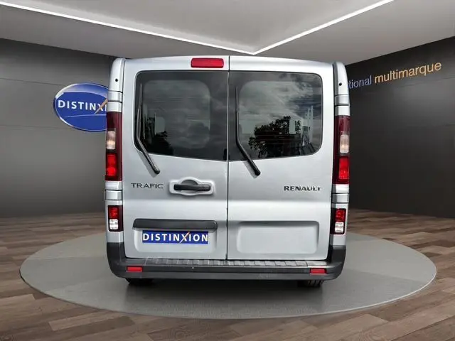Vue arrière d’un Renault Trafic Combi gris platine avec portes battantes et vitres teintées, en intérieur showroom.