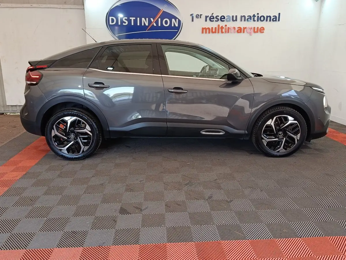 Profil droit d'une Citroën C4 2022 gris foncé avec jantes noires et détails chromés, en intérieur showroom.
