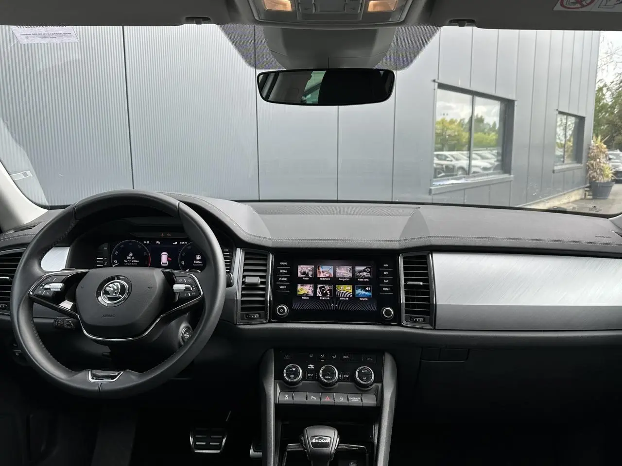 Vue intérieure du tableau de bord du Skoda Kodiaq blanc Glacier 2024, avec volant multifonction et écran tactile central allumé.