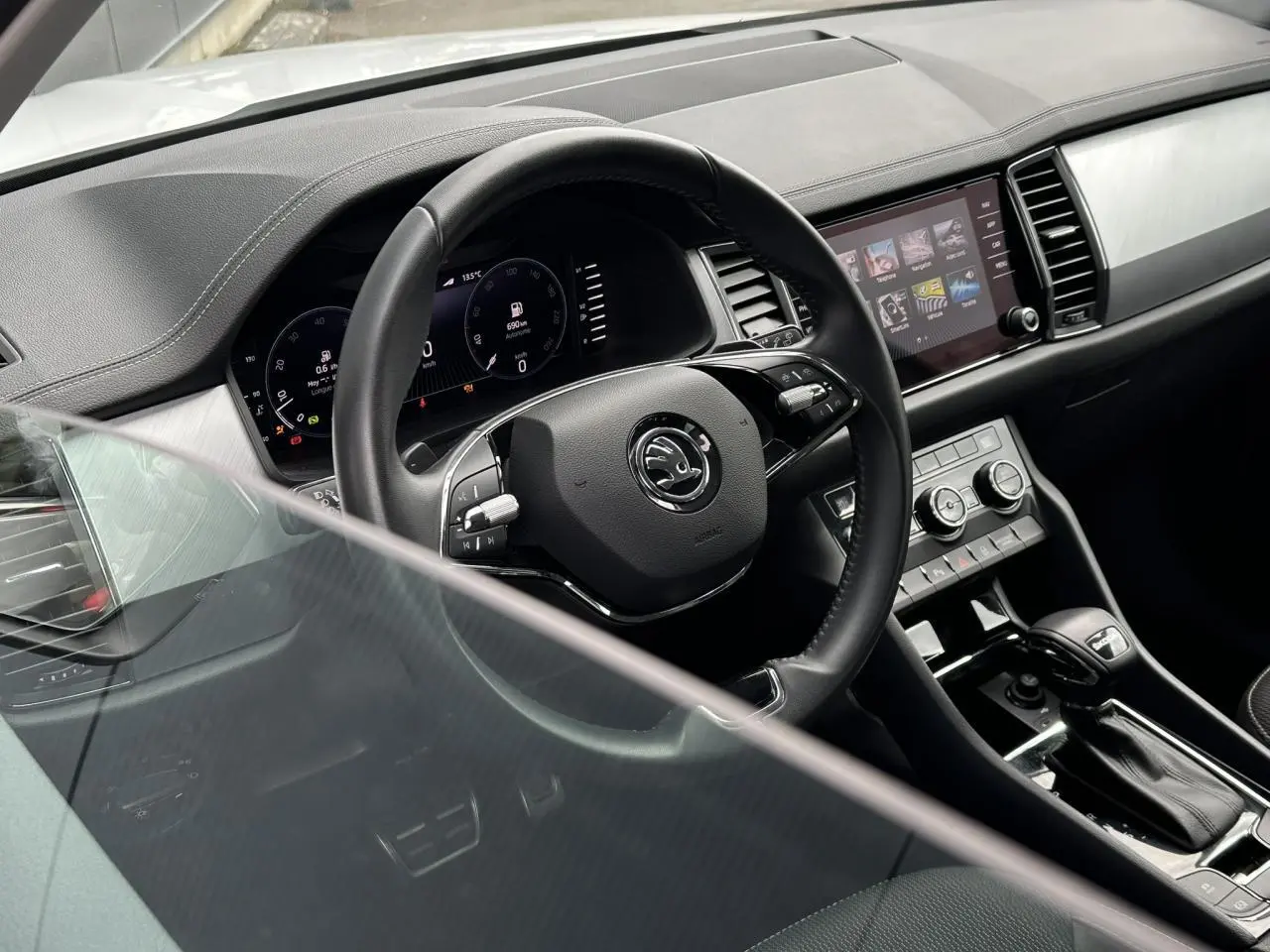 Vue intérieure du poste de conduite du Skoda Kodiaq blanc, mettant en valeur le volant multifonction et l'écran tactile central.