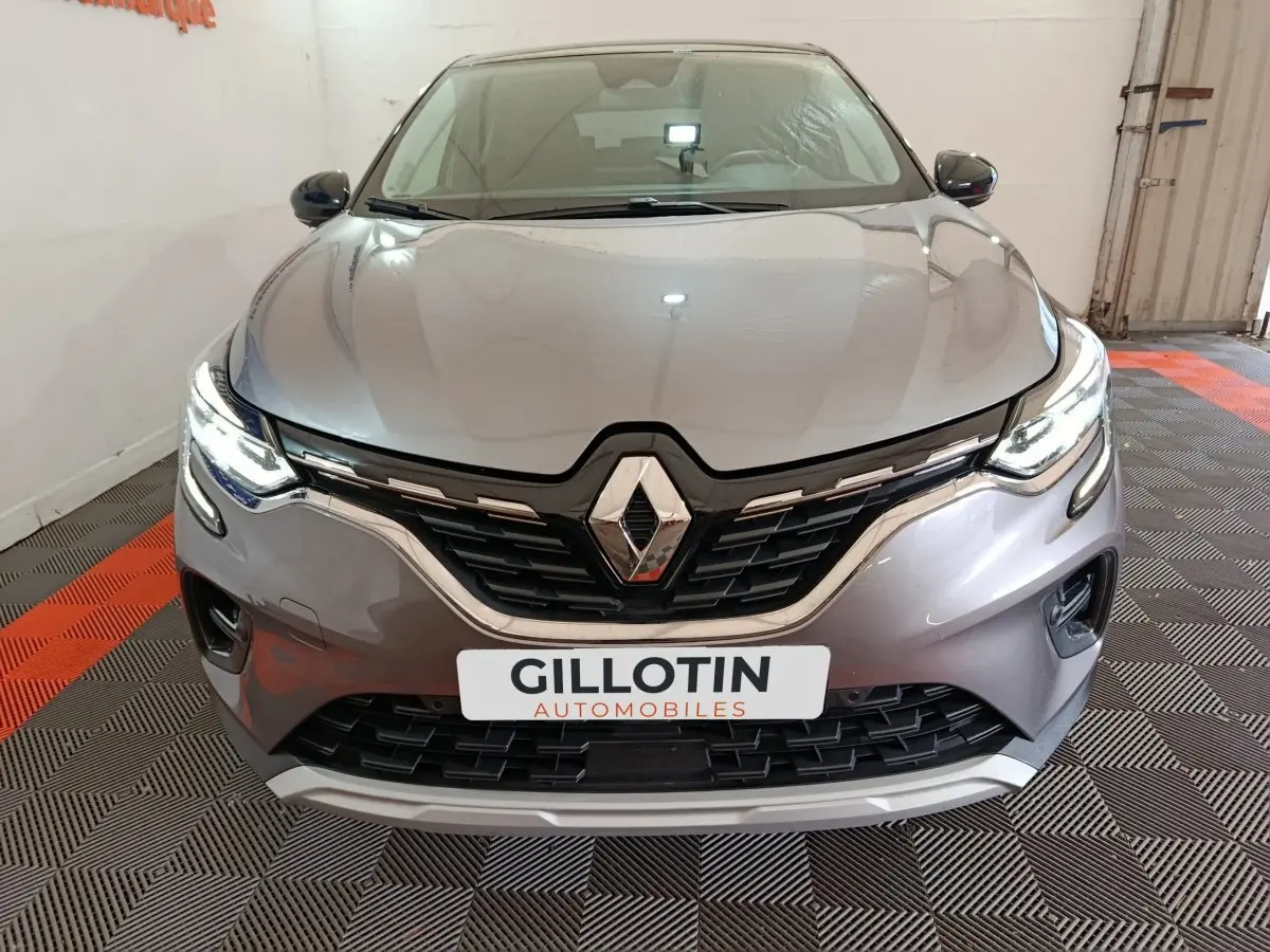 Vue frontale d'un Renault Captur gris foncé 2024 avec phares LED allumés et calandre noire brillante.