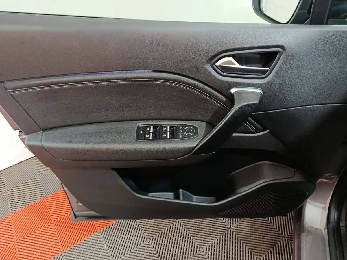 Vue du panneau de porte côté gauche gris foncé du Renault Captur 2024 avec commandes électriques des vitres et poignée noire.