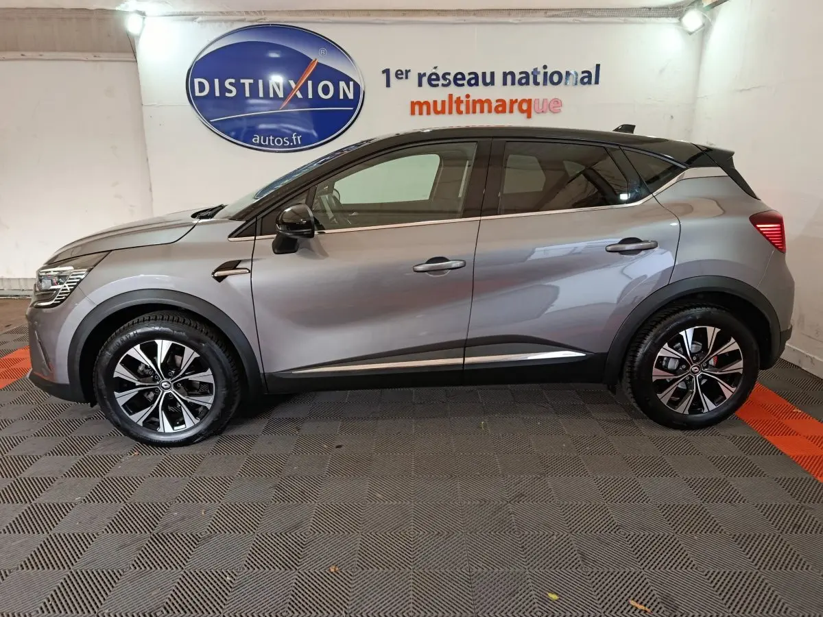 Profil côté gauche du Renault Captur Techno TCe 90 gris foncé 2024 avec jantes alliage et vitres teintées en intérieur showroom.