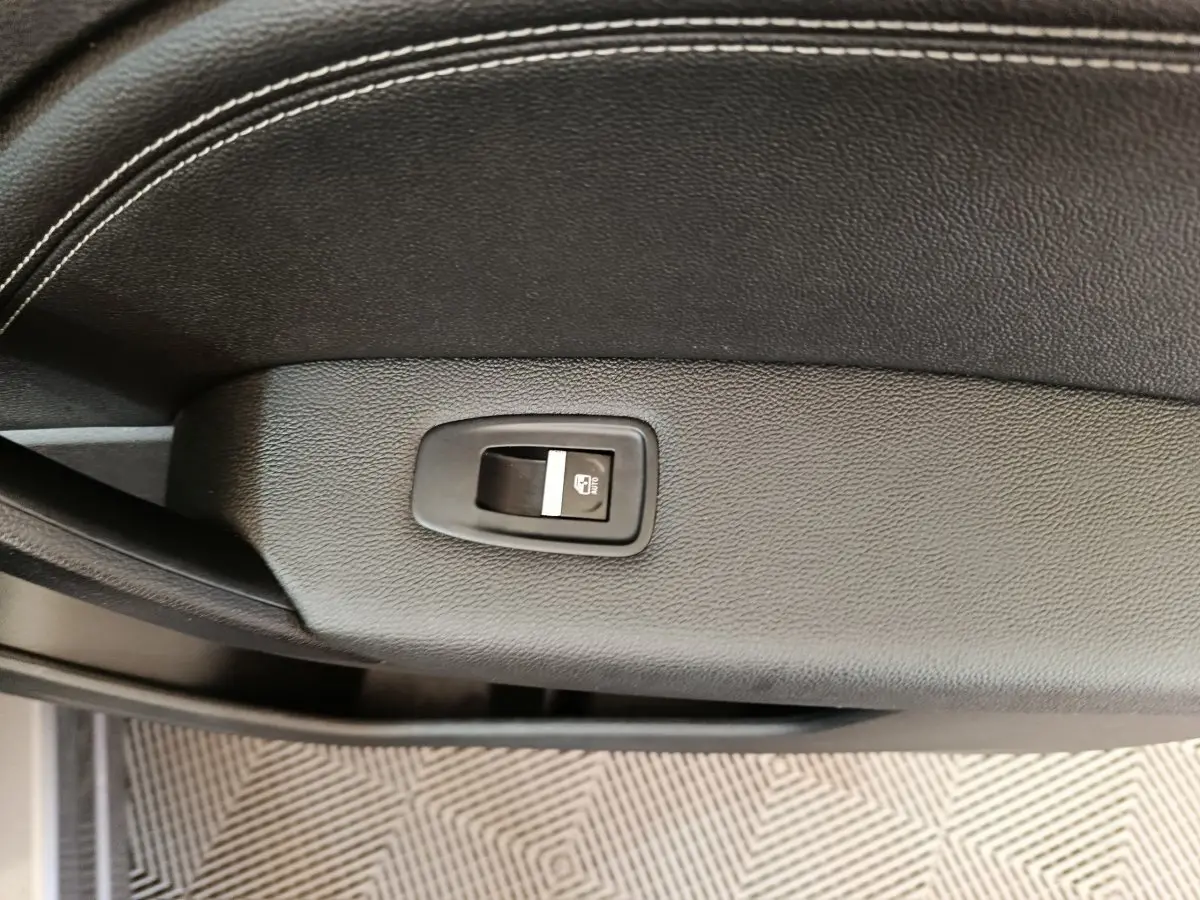 Gros plan sur le bouton de verrouillage des vitres sur la porte intérieure en cuir noir du Renault Captur gris foncé 2024.