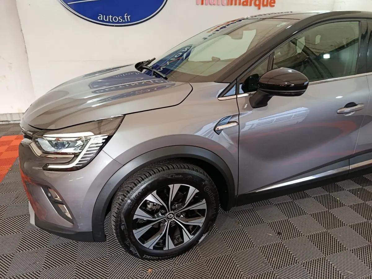 Vue de profil avant droit d'un Renault Captur 2024 gris foncé avec jante alliage et rétroviseur noir brillant.