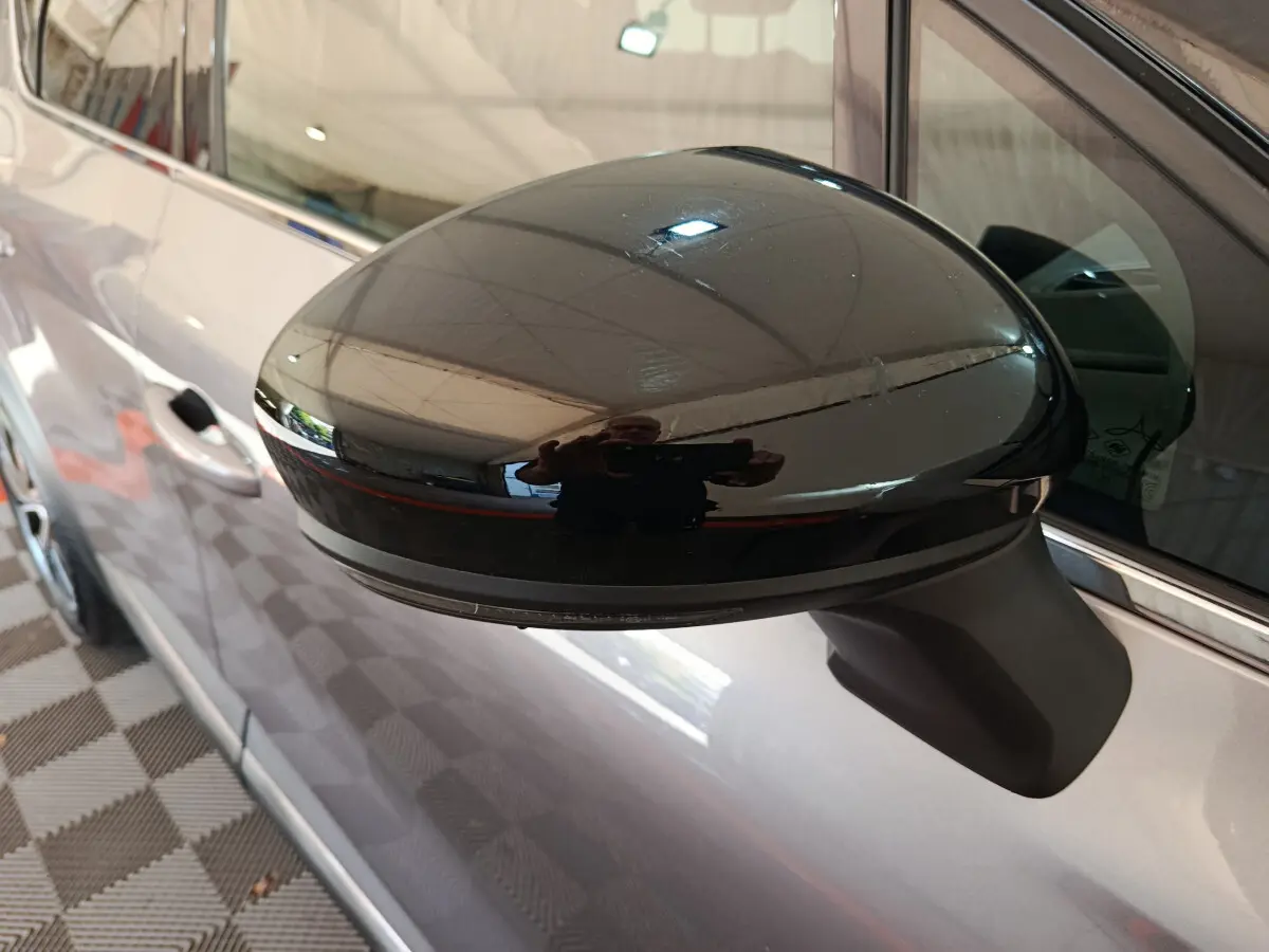Rétroviseur noir brillant côté gauche du Renault Captur gris foncé, avec reflet de l'environnement intérieur.