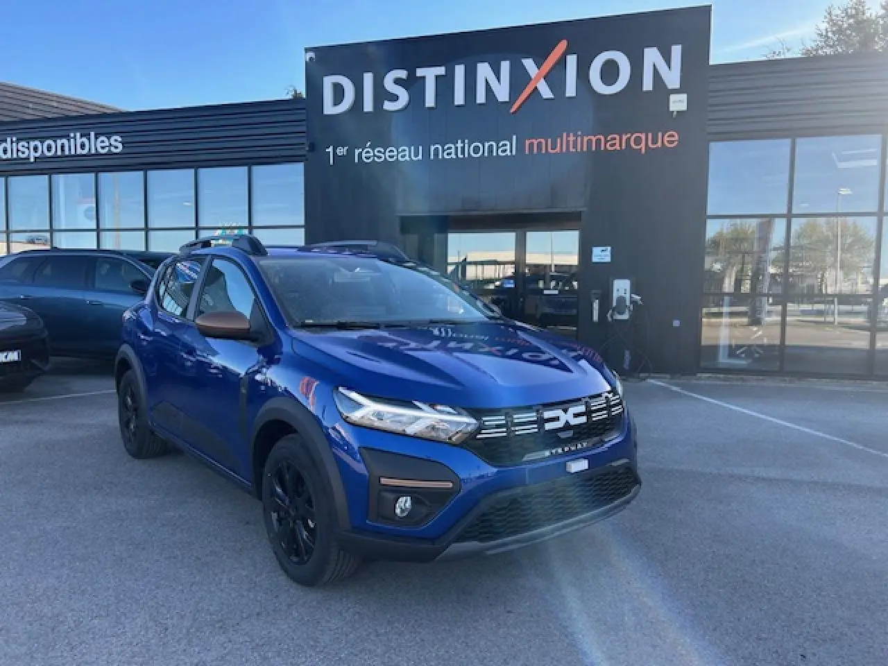 Dacia Sandero III Stepway bleu Iron en 3/4 avant droit, avec calandre noire et barres de toit brun cuivré.