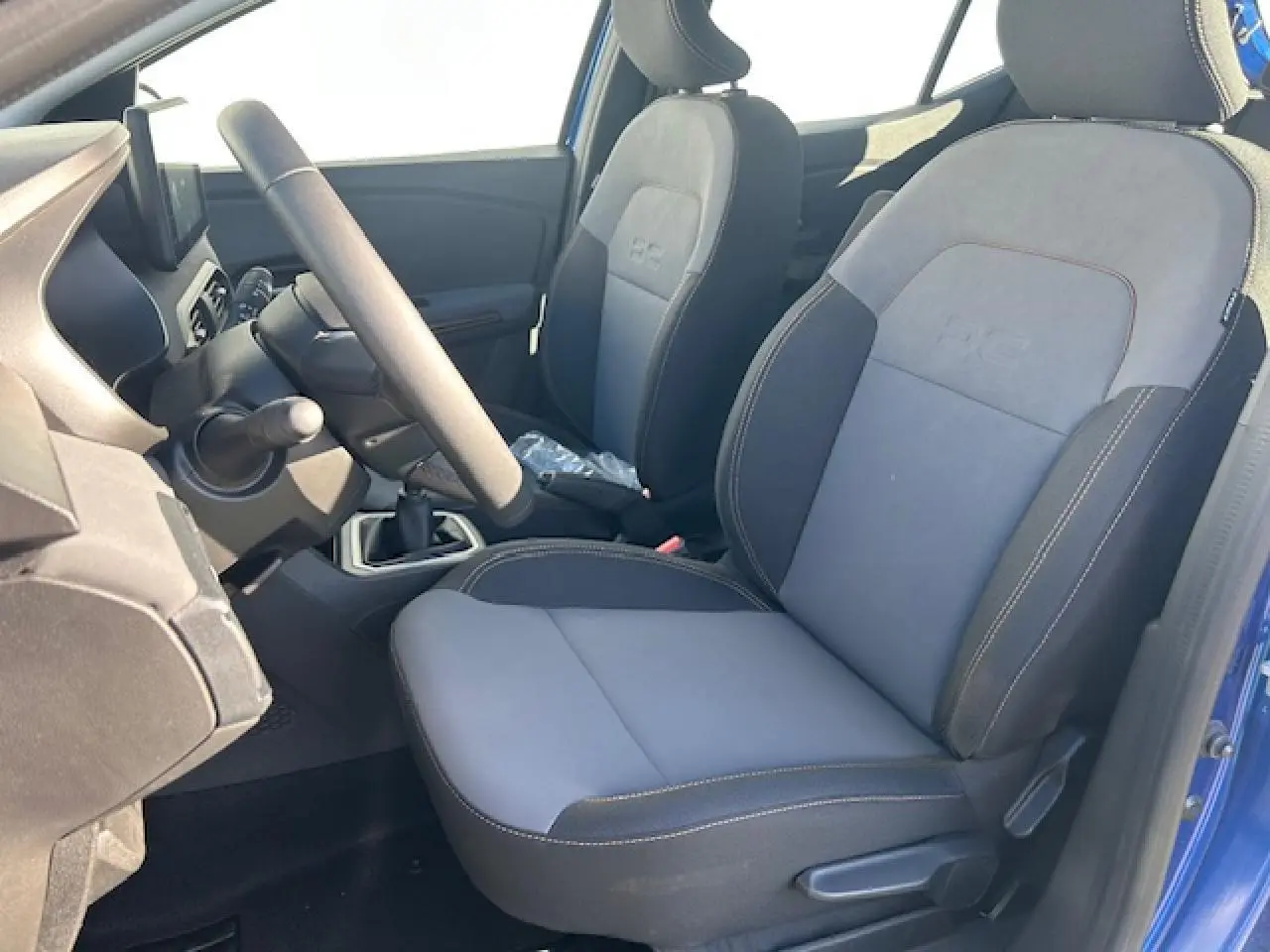 Vue intérieure côté conducteur de la Dacia Sandero III Stepway bleu Iron, sièges tissu gris avec logo DC brodé.