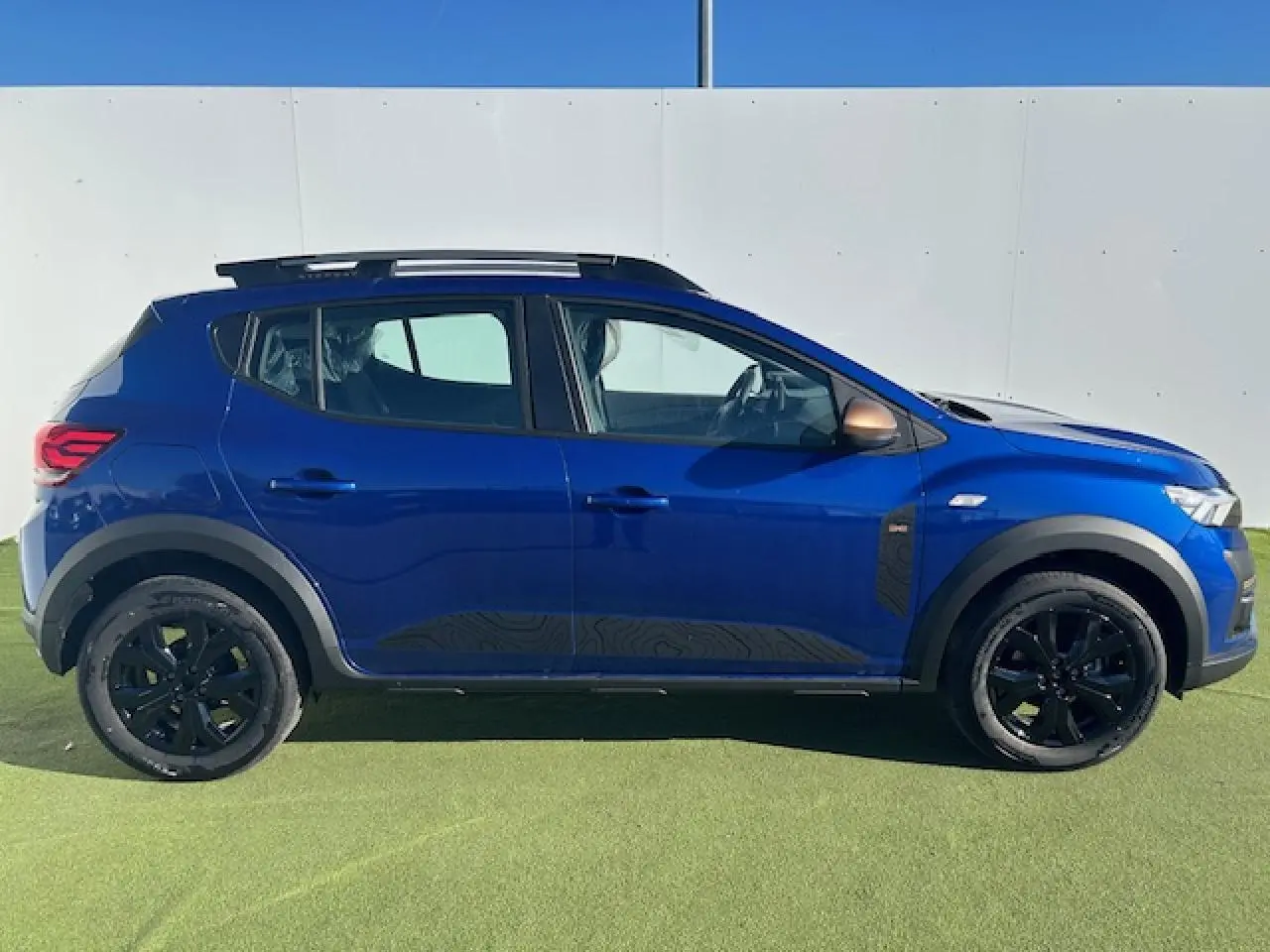 Profil côté gauche d'une Dacia Sandero Stepway bleu iron avec jantes noires et barres de toit grises sur fond clair.