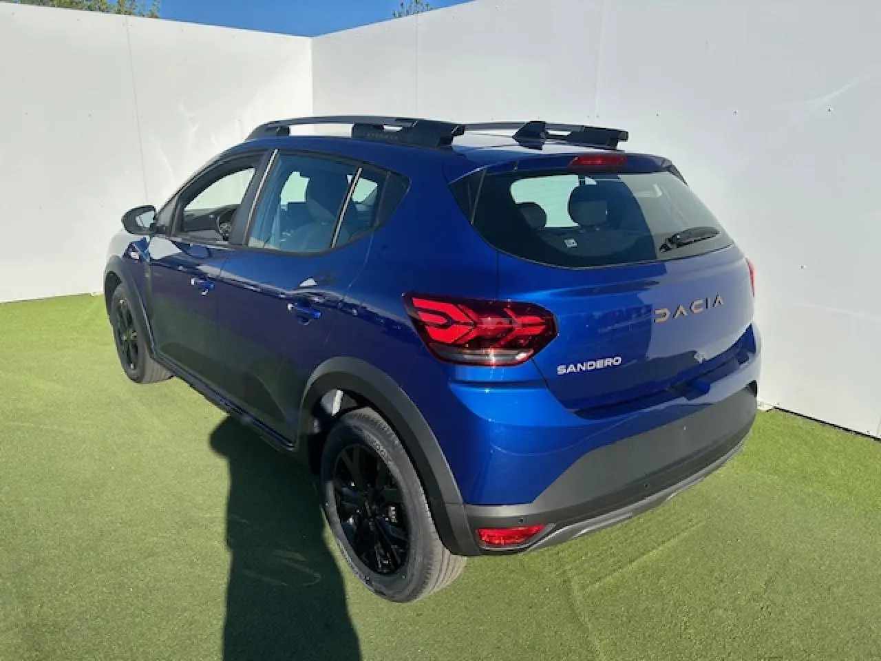 Vue 3/4 arrière droite d'une Dacia Sandero III Stepway bleu Iron avec jantes noires et barres de toit.