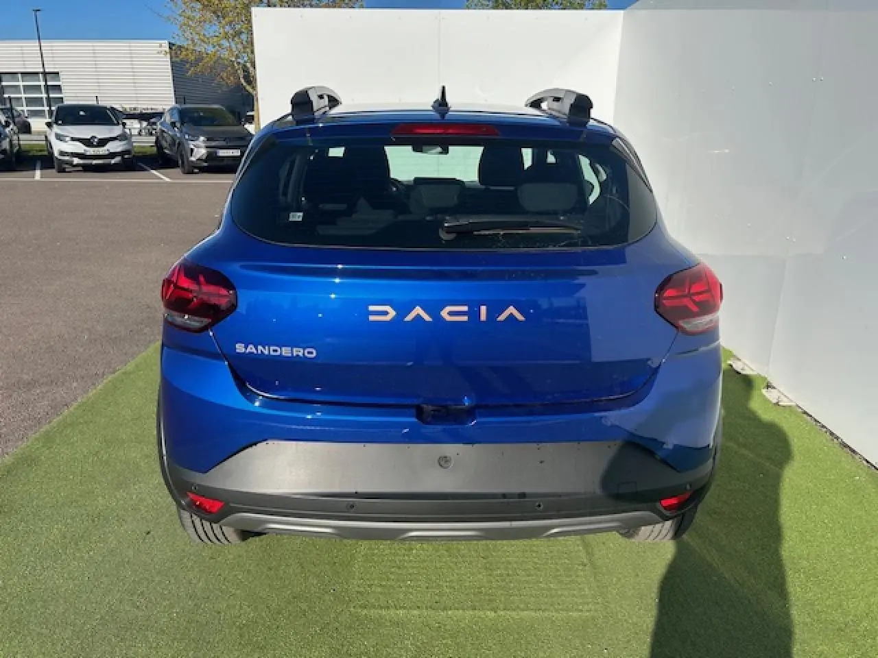 Vue arrière d'une Dacia Sandero III Stepway bleu Iron avec barres de toit et logo Dacia brun cuivré.