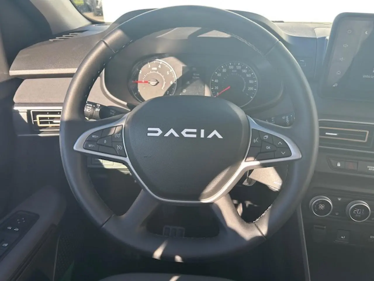 Vue centrée sur le volant noir du Dacia Sandero 2025 avec tableau de bord et commandes visibles en arrière-plan.