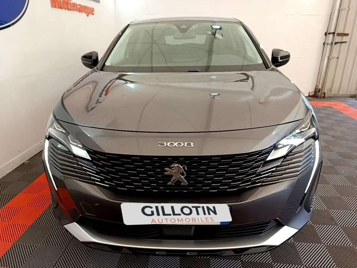 Vue frontale d'un Peugeot 3008 gris foncé avec calandre noire et éclairage LED distinctif en intérieur showroom.