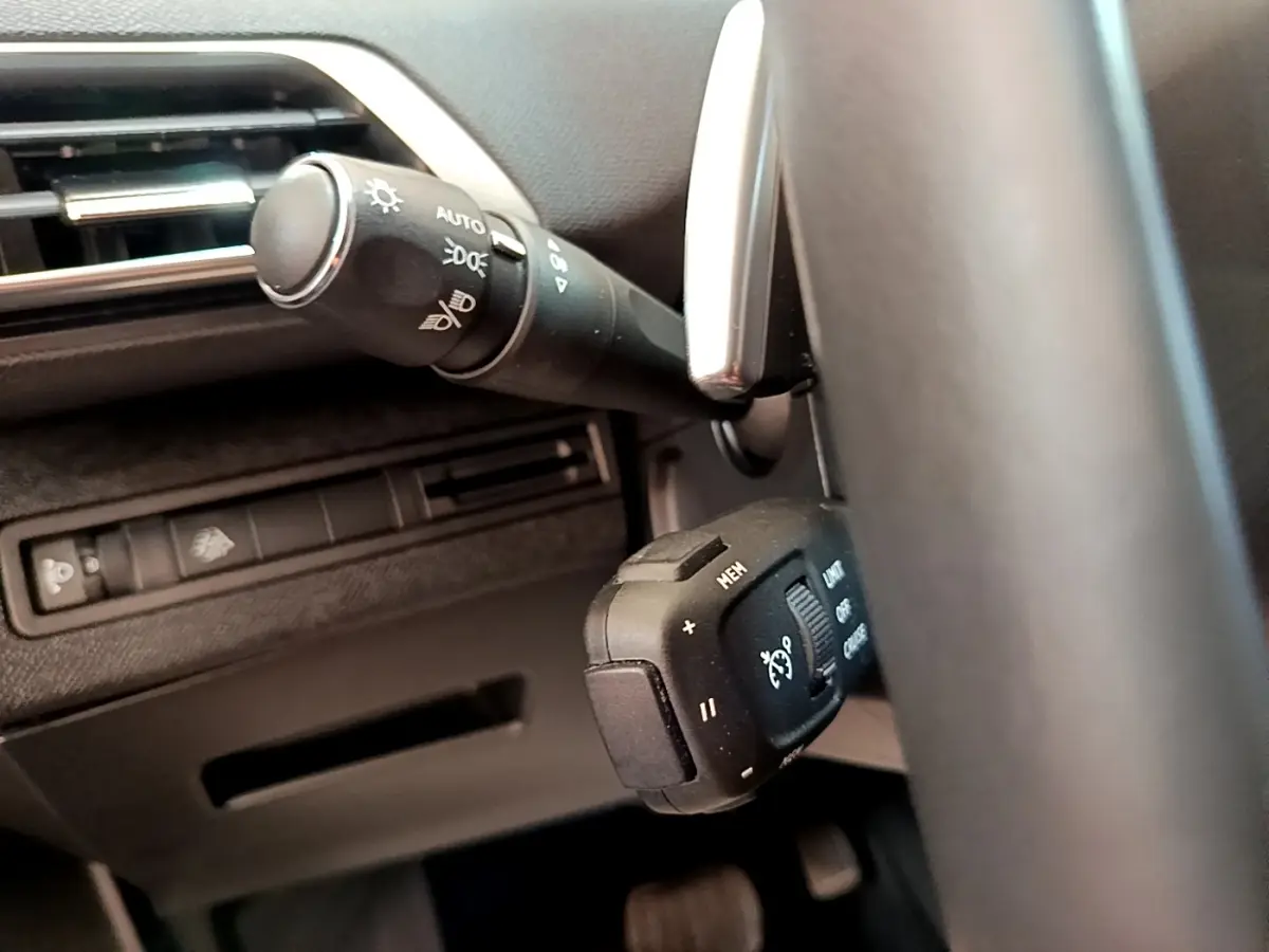 Gros plan sur la commande de régulateur de vitesse et éclairage côté gauche du volant d’un Peugeot 3008 gris foncé 2022.
