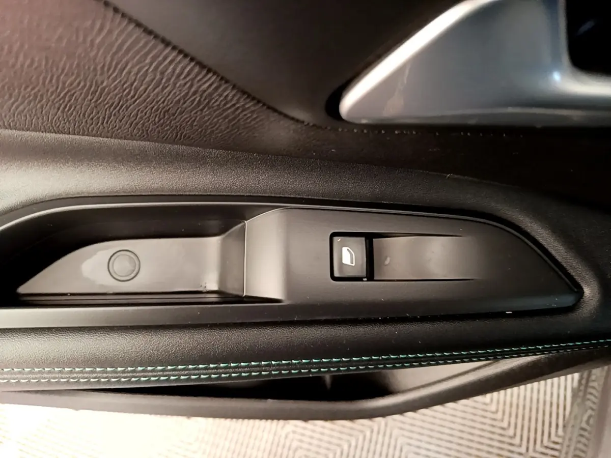 Gros plan sur la commande de lève-vitre côté gauche du Peugeot 3008 gris foncé, avec surpiqûres bleues visibles.
