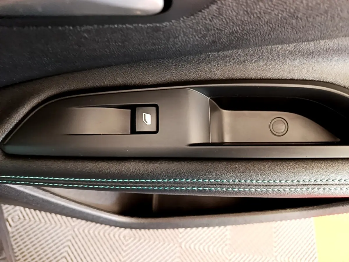 Gros plan sur la commande de lève-vitre et la poignée intérieure côté gauche d’une Peugeot 3008 gris foncé.