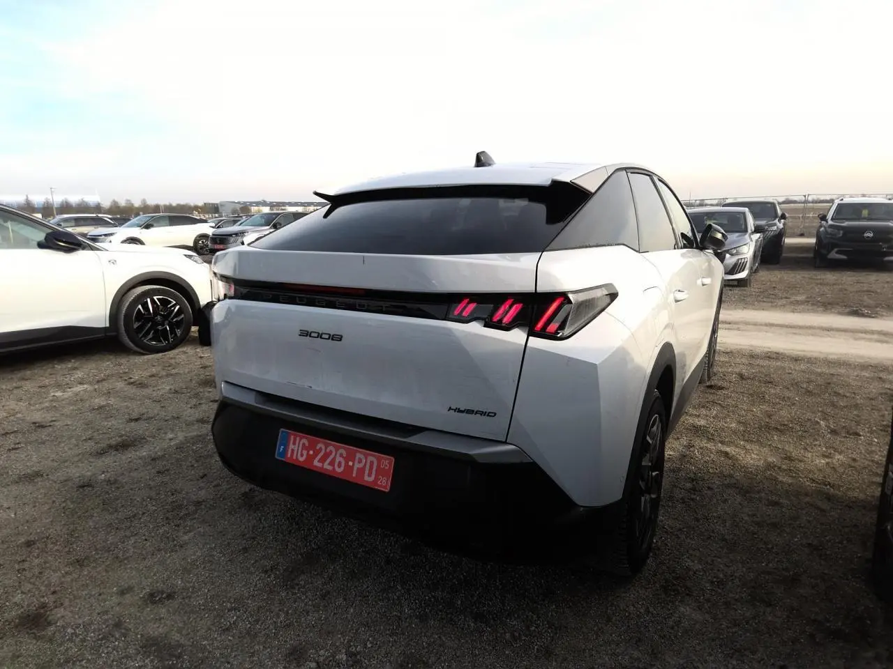 Vue 3/4 arrière droite d'un Peugeot 3008 hybride blanc avec feux arrière LED à griffes et bandeau noir laqué.