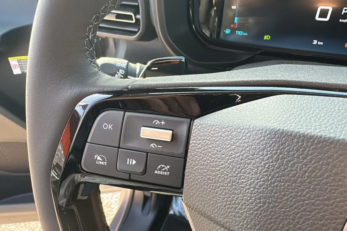 Gros plan sur les commandes au volant gauche du Citroën Berlingo 2025 gris artense, avec affichage numérique en arrière-plan.