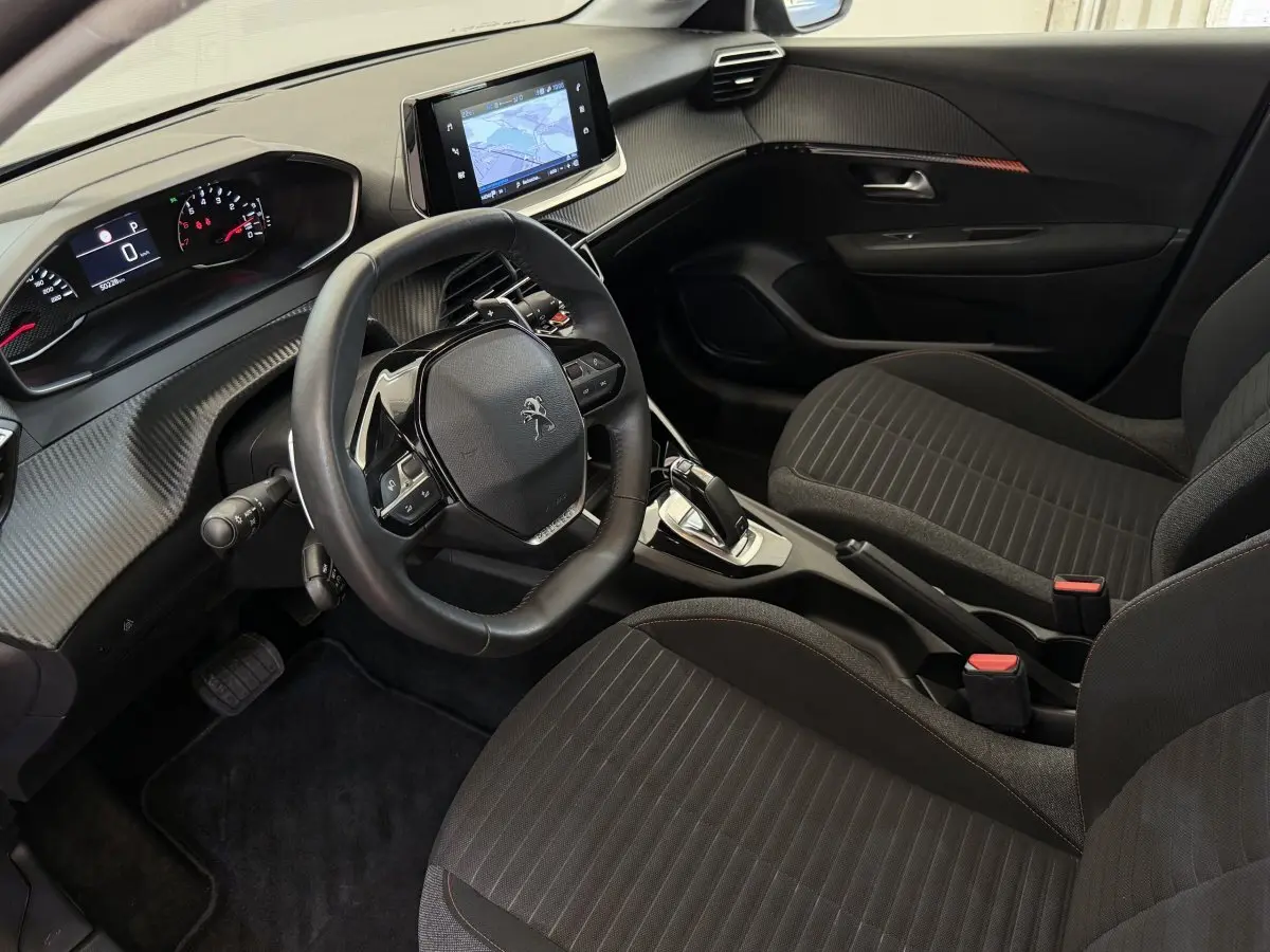 Intérieur noir de la Peugeot 208 PureTech 100, vue côté conducteur, volant cuir et écran tactile central visible.