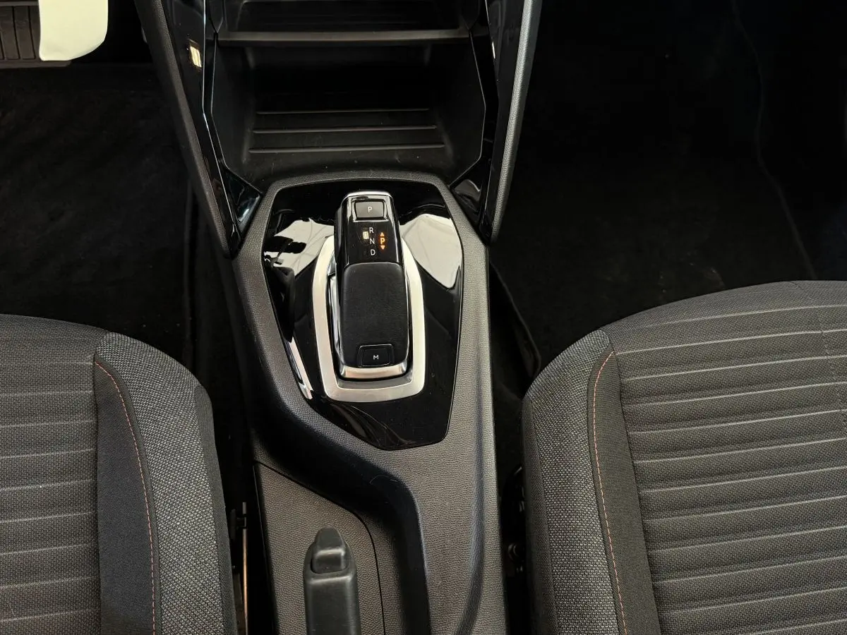 Le levier de vitesse de la Peugeot 208 PureTech noir, vu de dessus entre les sièges avant en tissu gris.