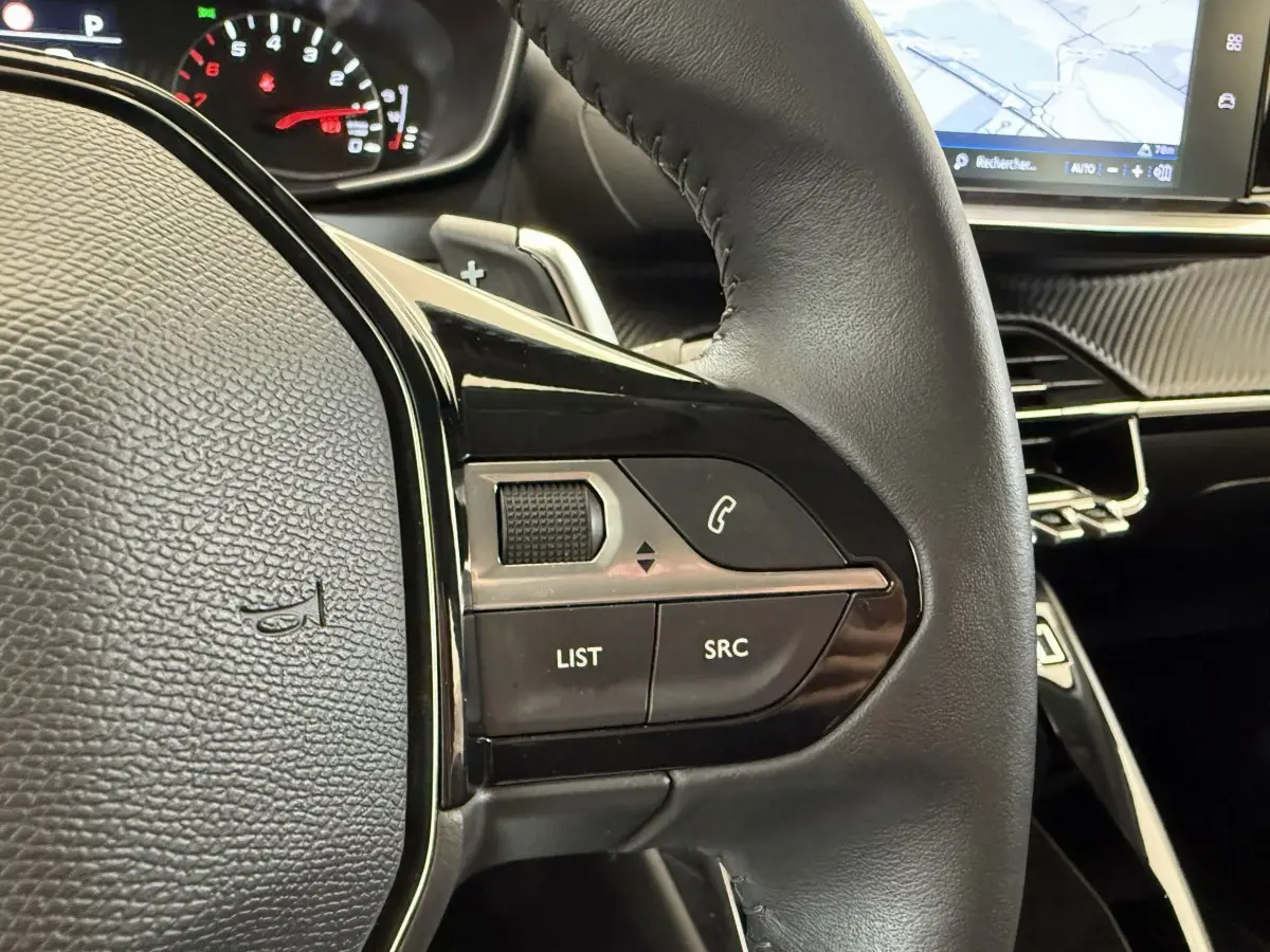Gros plan sur le volant cuir noir de la Peugeot 208 2021 avec commandes audio et tableau de bord numérique.