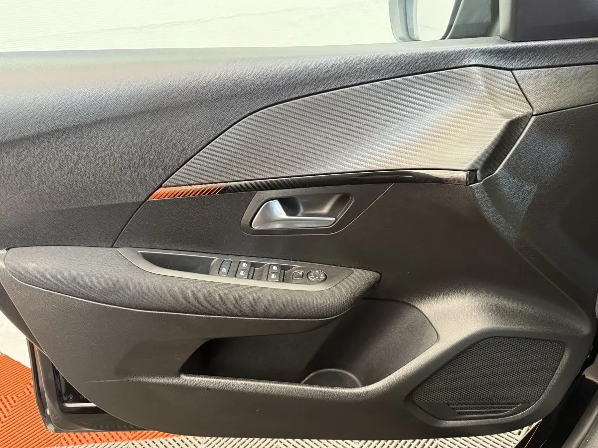 Gros plan sur la porte côté conducteur noire de la Peugeot 208 2021 avec insert effet carbone et commandes électriques.