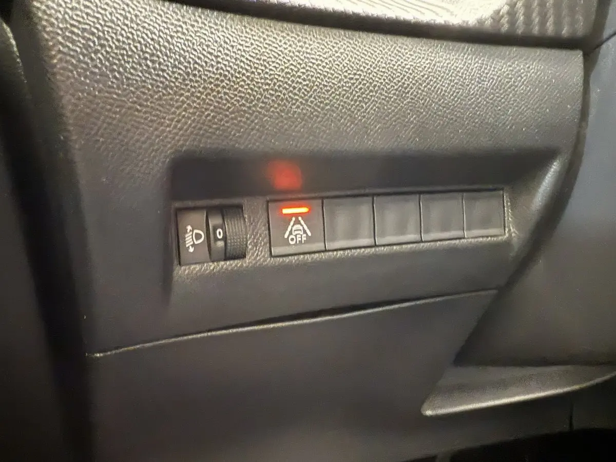 Gros plan sur les commandes de réglage des phares et désactivation de l'assistance au maintien de voie dans une Peugeot 208 noire 2021.