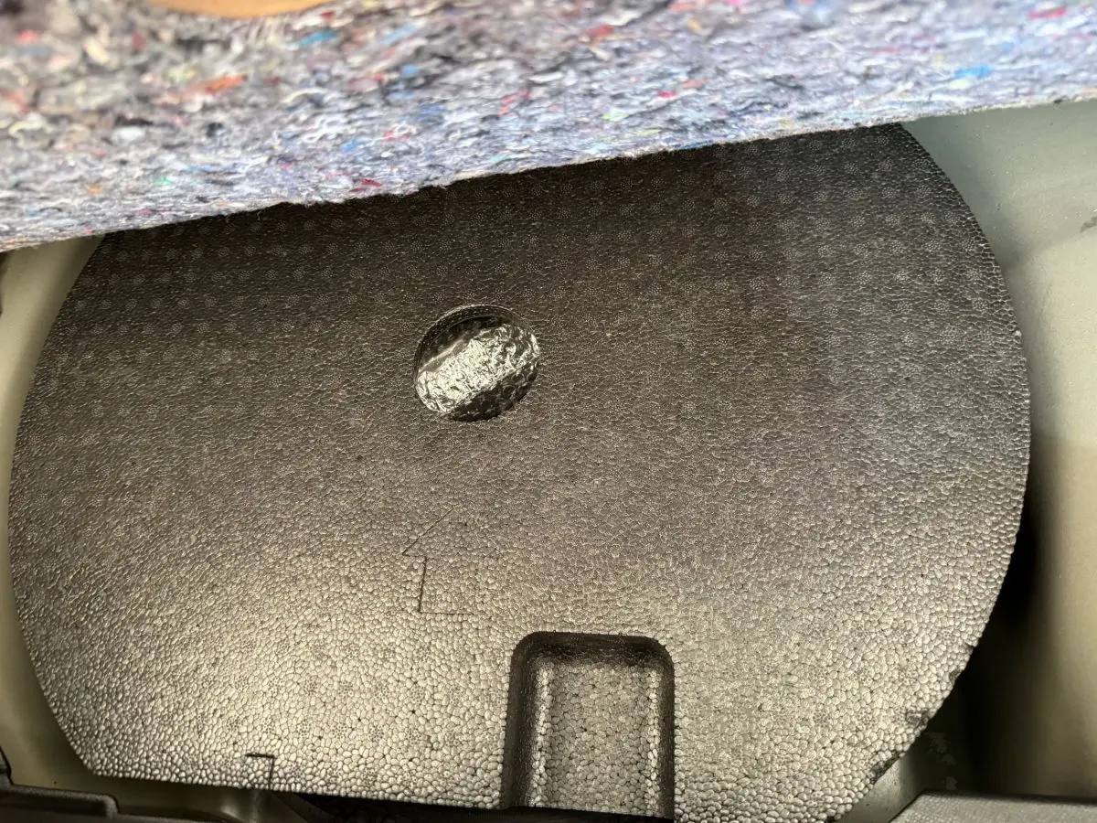 Coffre ouvert d'une Peugeot 208 noire, vue plongeante sur la protection en mousse du logement de la roue de secours.