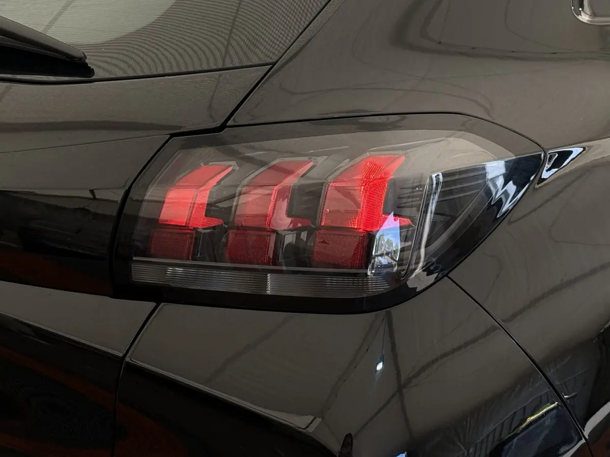 Gros plan sur le feu arrière droit rouge d'une Peugeot 208 noire, soulignant la finition lisse et brillante du véhicule.