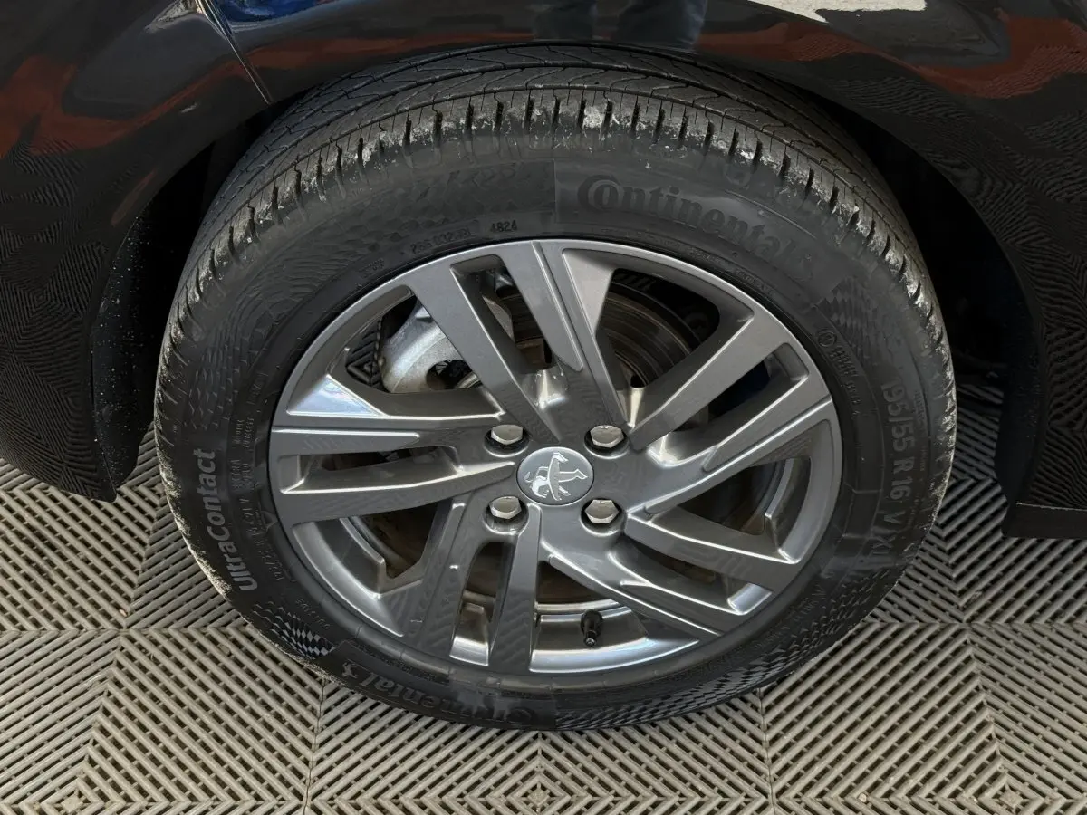 Gros plan sur la roue avant gauche noire d'une Peugeot 208 2021 avec jante alliage gris et logo lion central.