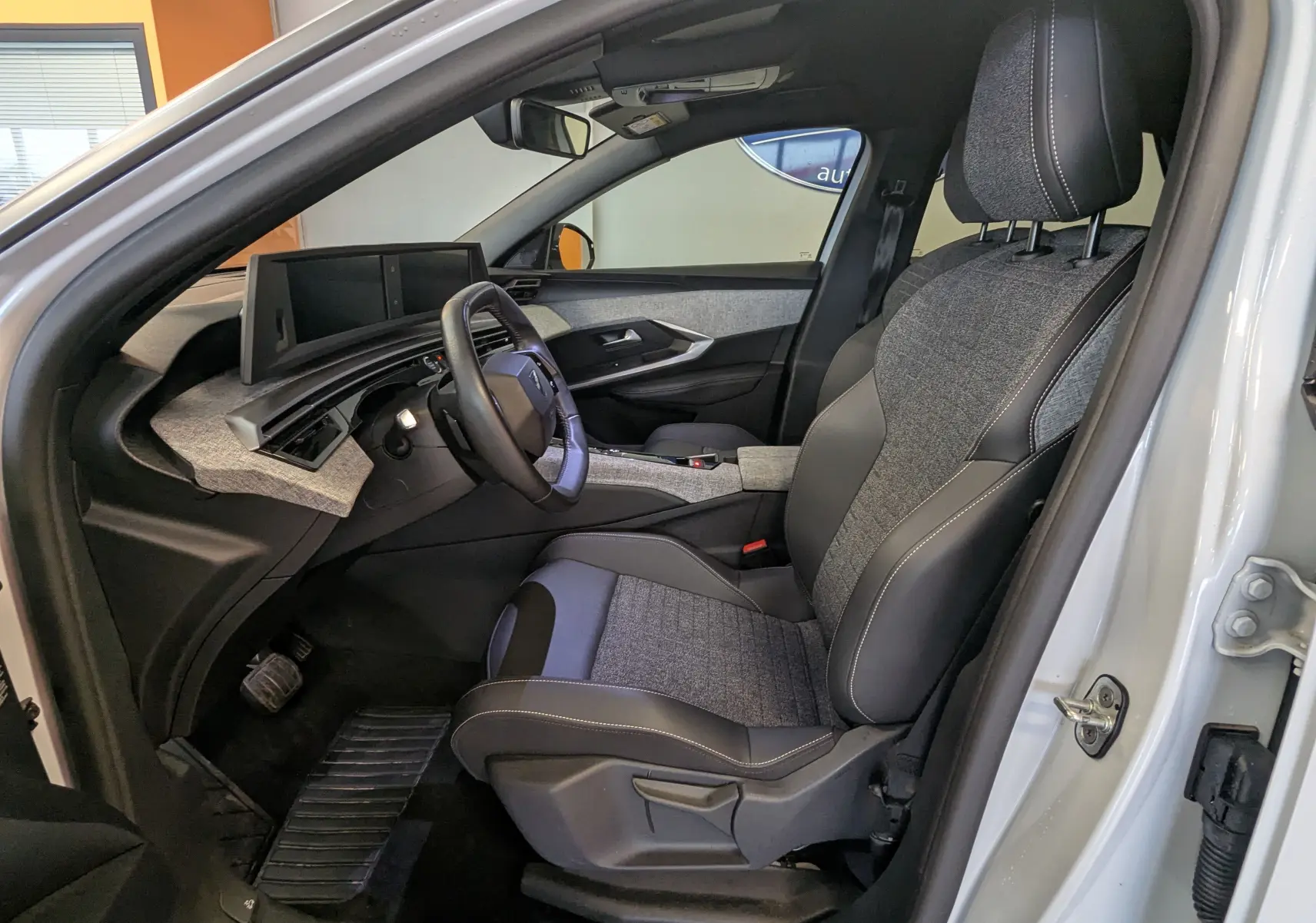 Vue intérieure côté conducteur du Peugeot 3008 Hybrid blanc 2025, avec sellerie tissu gris et volant cuir.