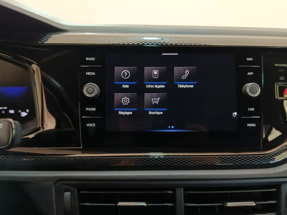 Écran tactile central du tableau de bord du Volkswagen Taigo gris foncé, affichant le menu principal avec options d’aide et téléphone.