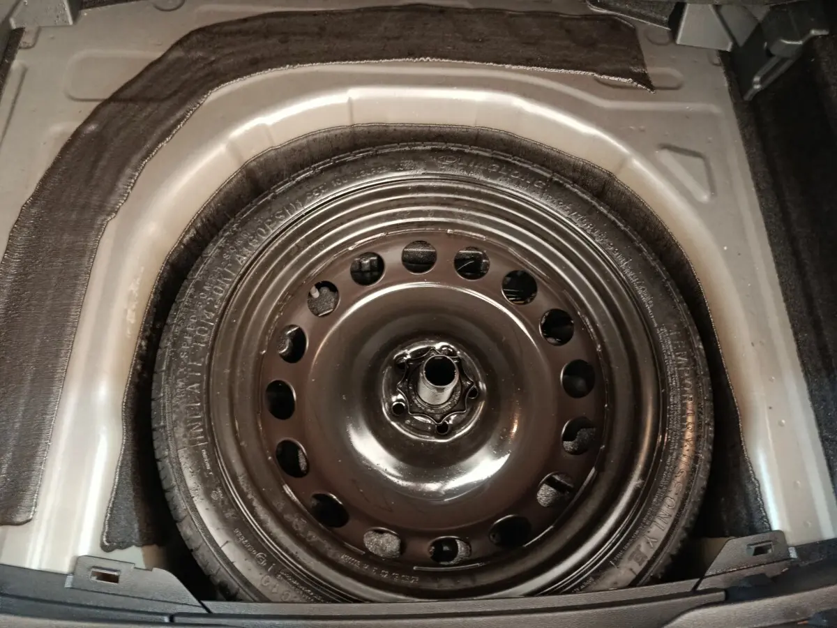 Gros plan sur la roue de secours galette en jante acier dans le coffre du Volkswagen Taigo gris foncé 2023.