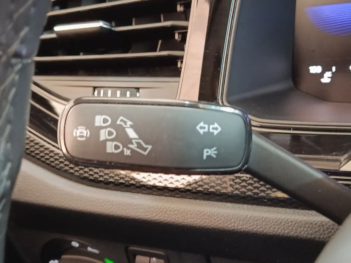 Gros plan sur la commande de clignotants et feux, tableau de bord partiellement visible du Volkswagen Taigo gris foncé.