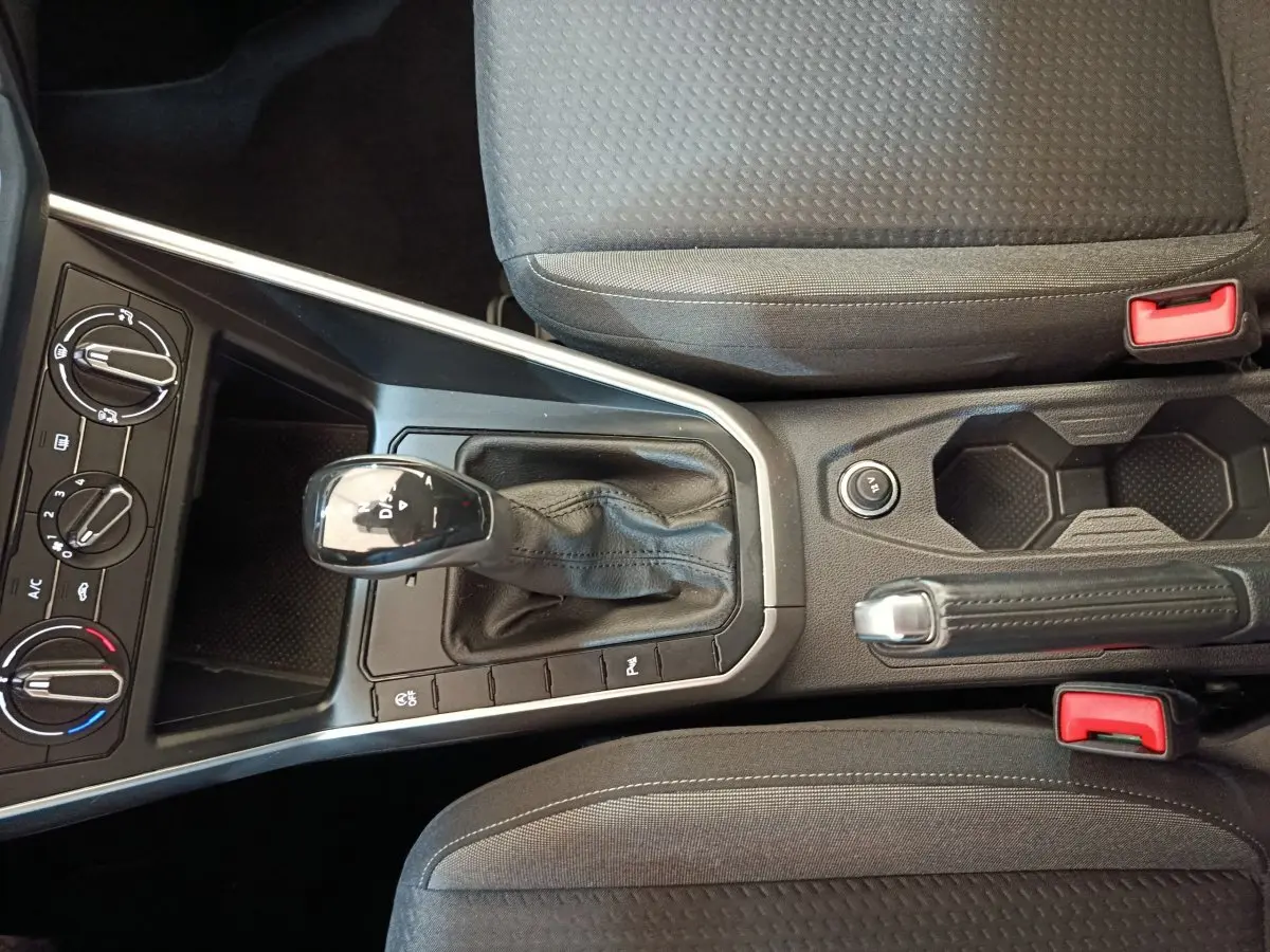 Vue intérieure centrée sur la console centrale du Volkswagen Taigo gris foncé avec levier de vitesse automatique et frein à main.