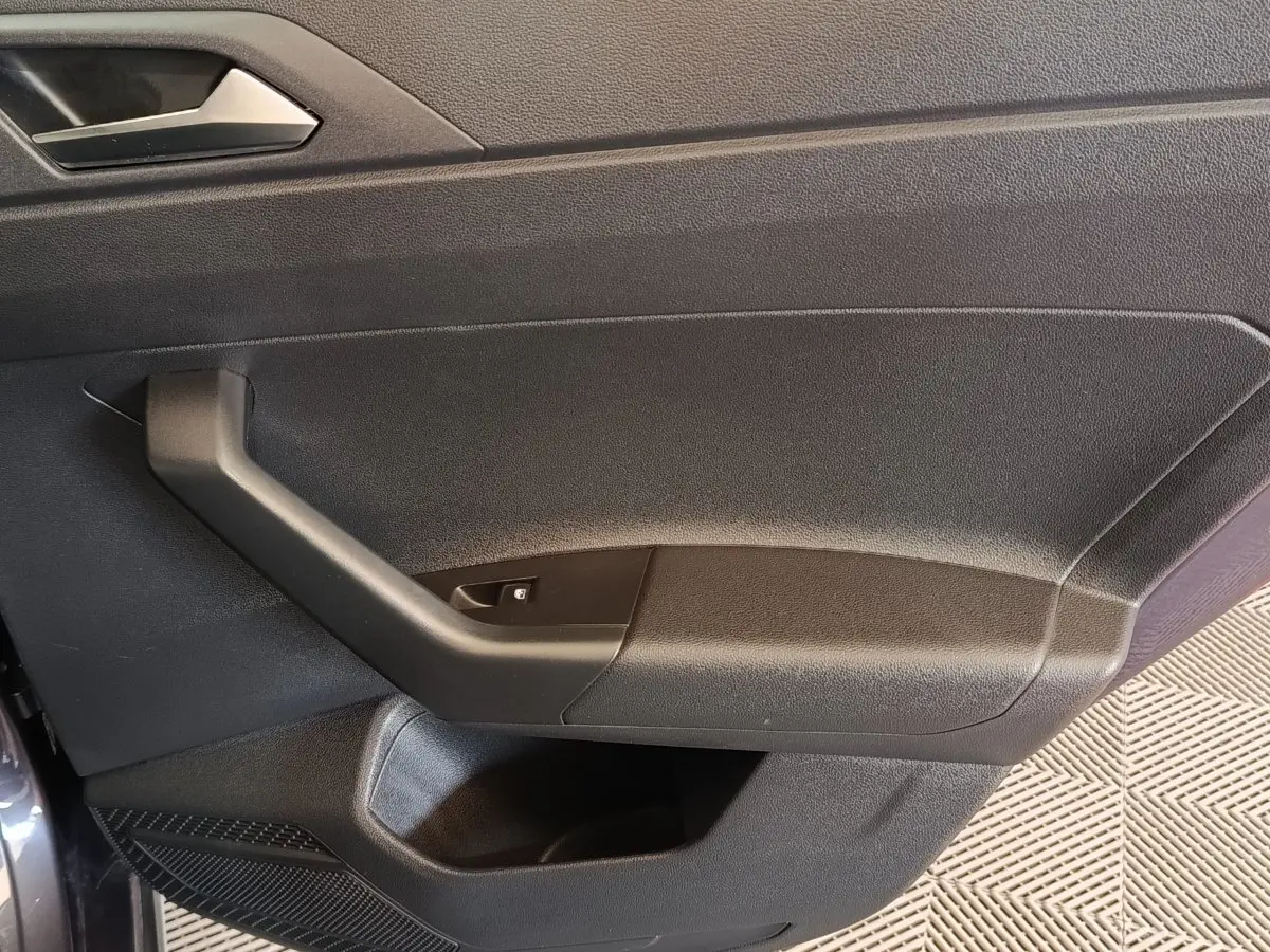 Gros plan sur la porte intérieure côté gauche du Volkswagen Taigo gris foncé, montrant la poignée et le bouton de lève-vitre.