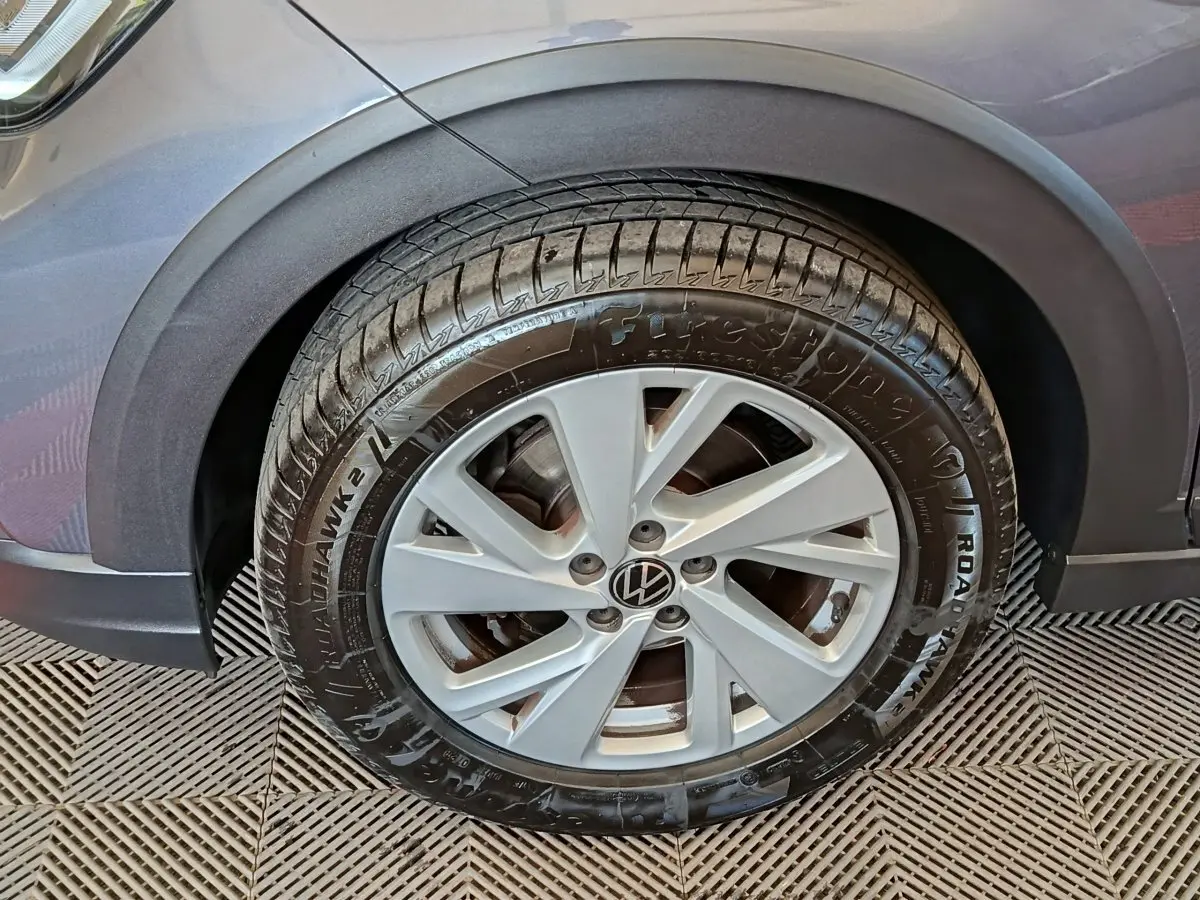 Gros plan sur la roue avant gauche d’un Volkswagen Taigo gris foncé, mettant en valeur la jante et le pneu Firestone.
