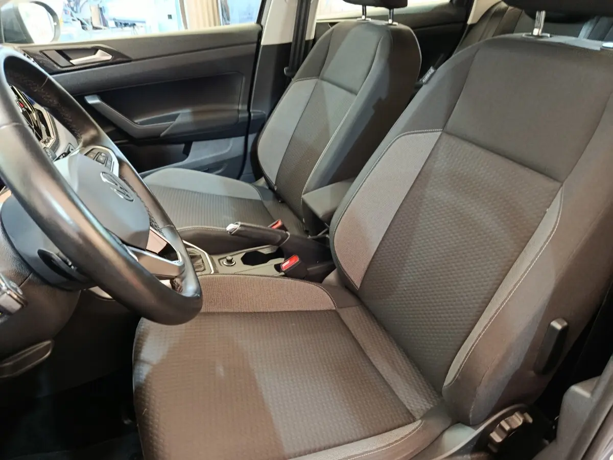 Vue intérieure côté conducteur du Volkswagen Taigo 2023, sièges tissu gris foncé avec volant et console centrale visibles.