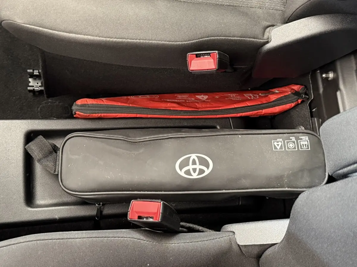 Vue intérieure centrée sur la console entre les sièges avant d’un Toyota Proace City blanc, avec trousse de secours noire et rouge.
