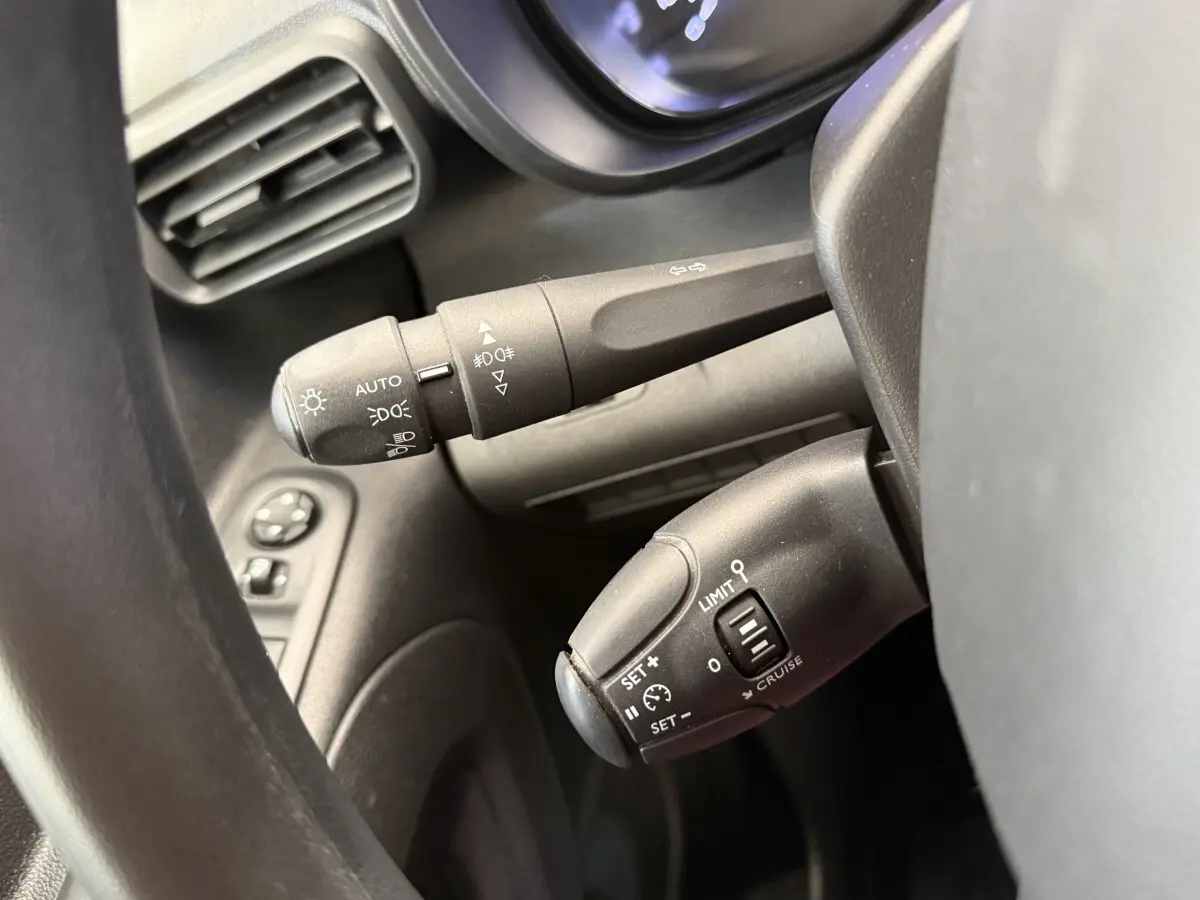 Gros plan sur les commandes au volant noir du Toyota Proace City blanc, montrant les réglages des phares et du régulateur de vitesse.
