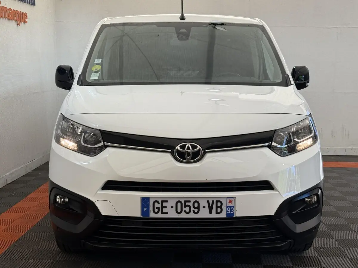 Vue frontale d'un Toyota Proace City blanc avec phares allumés et calandre noire dans un garage.