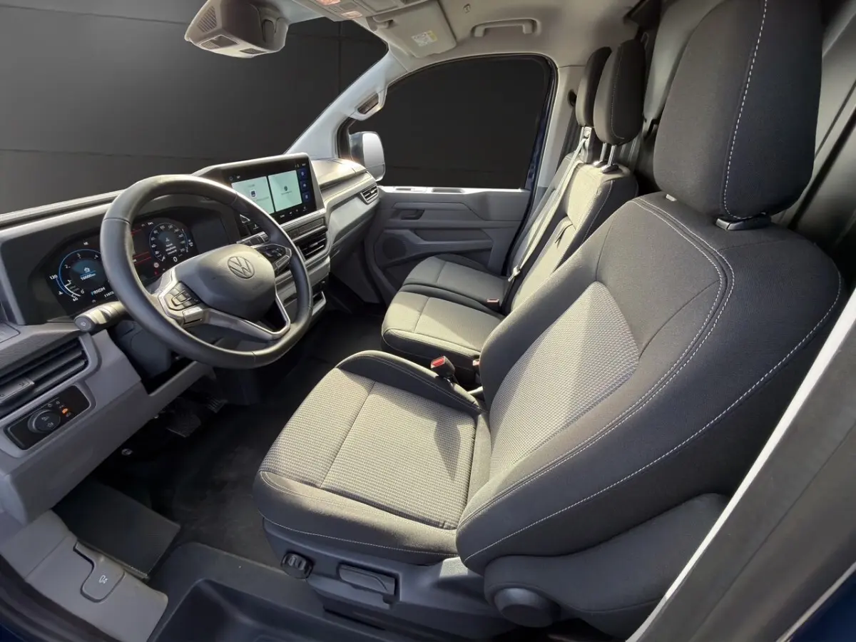 Vue intérieure côté conducteur du Volkswagen Transporter 2025 avec sièges gris et tableau de bord digital.