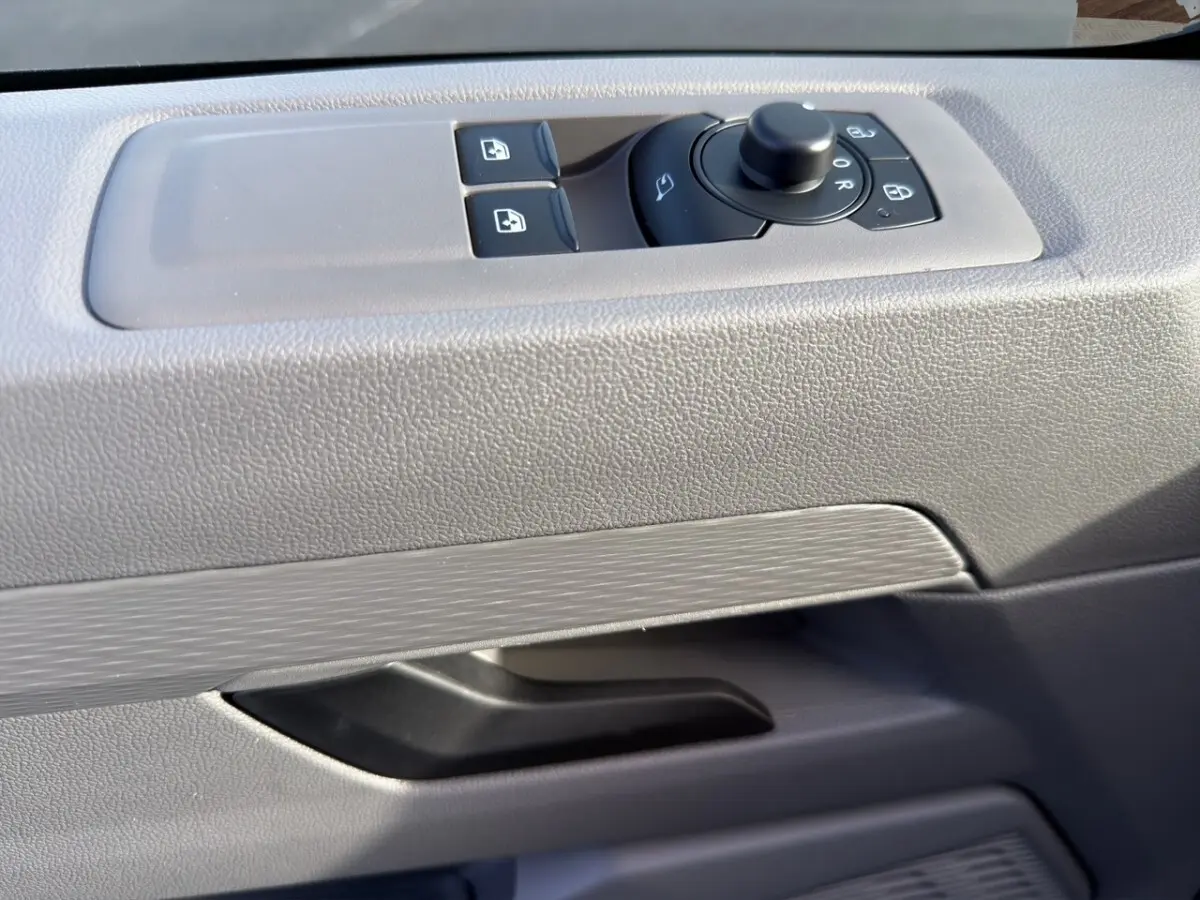 Détail de la commande des rétroviseurs et vitres sur la porte intérieure grise du Volkswagen Transporter 2025.