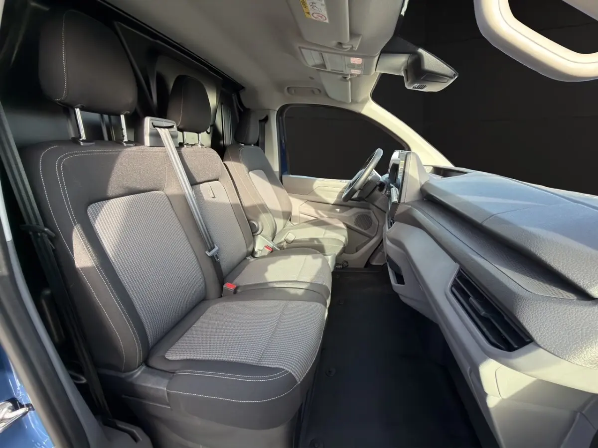 Vue intérieure côté conducteur du Volkswagen Transporter bleu 2025, montrant les sièges avant et le tableau de bord.