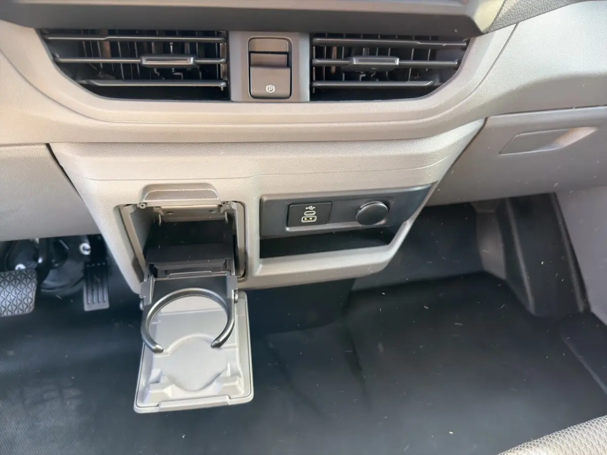 Détail intérieur du tableau de bord beige du Volkswagen Transporter 2025 avec porte-gobelet déployé et commande électrique.