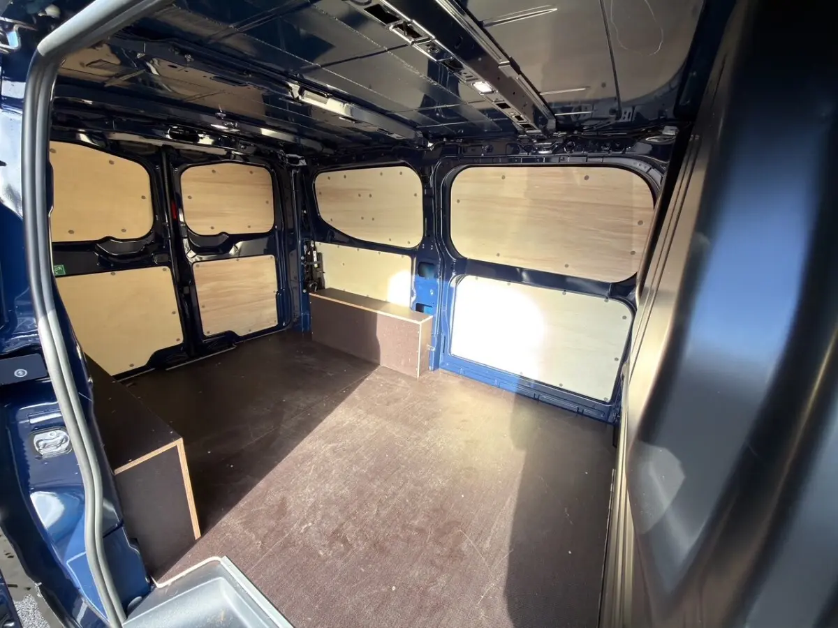 Vue intérieure arrière du Volkswagen Transporter bleu 2025 avec aménagement bois et espace de chargement vide.