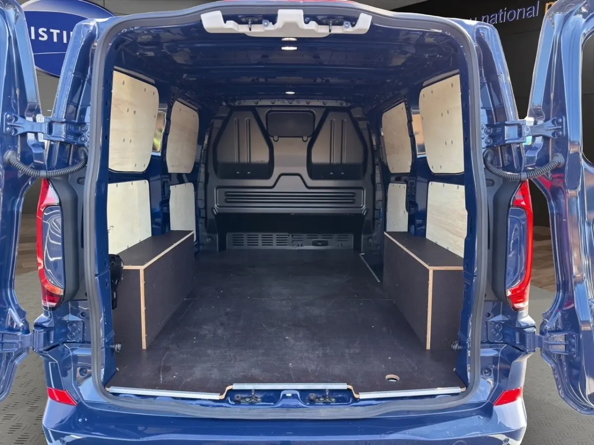 Vue arrière du Volkswagen Transporter bleu 2025 avec portes ouvertes montrant l'aménagement bois intérieur du coffre.