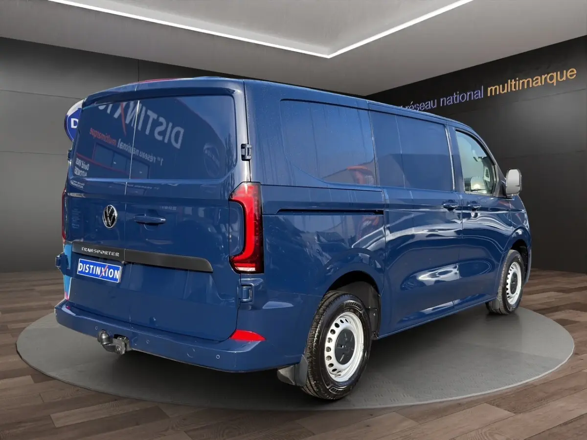 Vue 3/4 arrière droite du Volkswagen Transporter bleu avec attelage et jantes acier blanches en showroom.