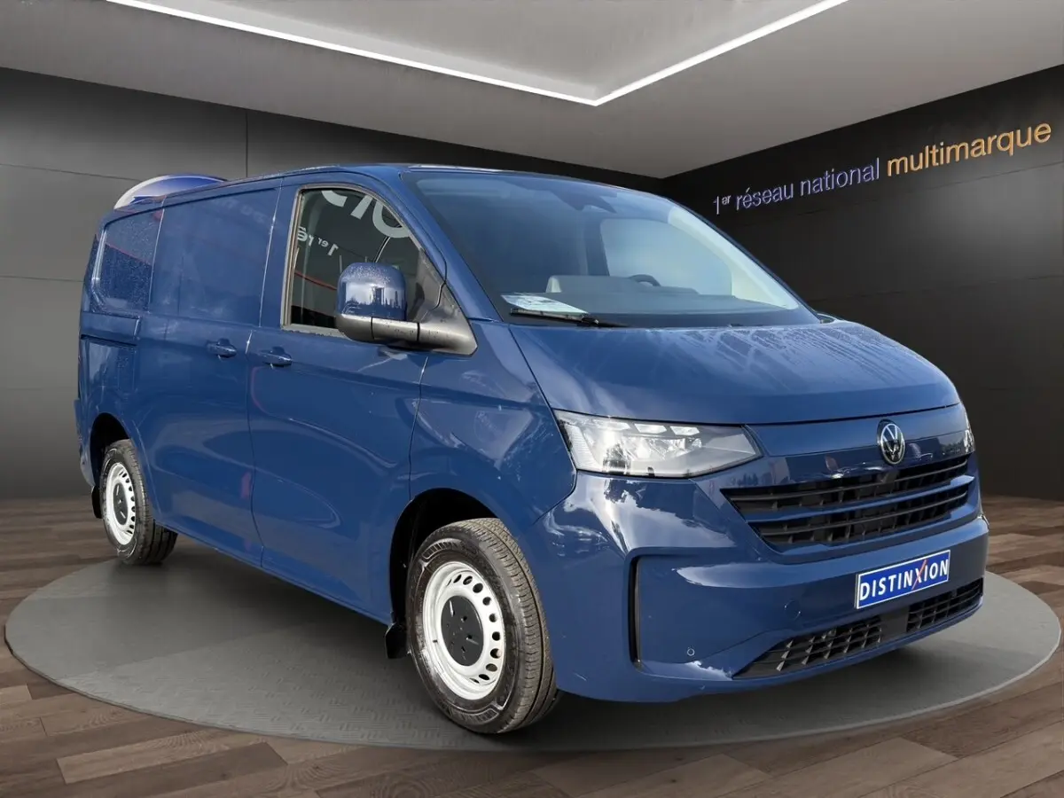 Vue 3/4 avant d’un Volkswagen Transporter bleu avec jantes acier et calandre noire, en intérieur showroom.