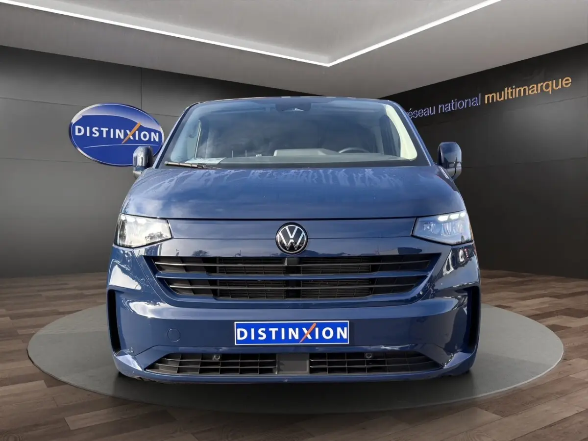 Vue frontale d'un Volkswagen Transporter bleu 2025 avec calandre noire et logo VW centré, en showroom.